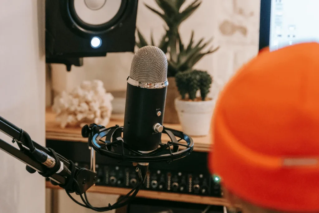 Studio microphone on an adjustable boom arm with a speaker and plants in the background.