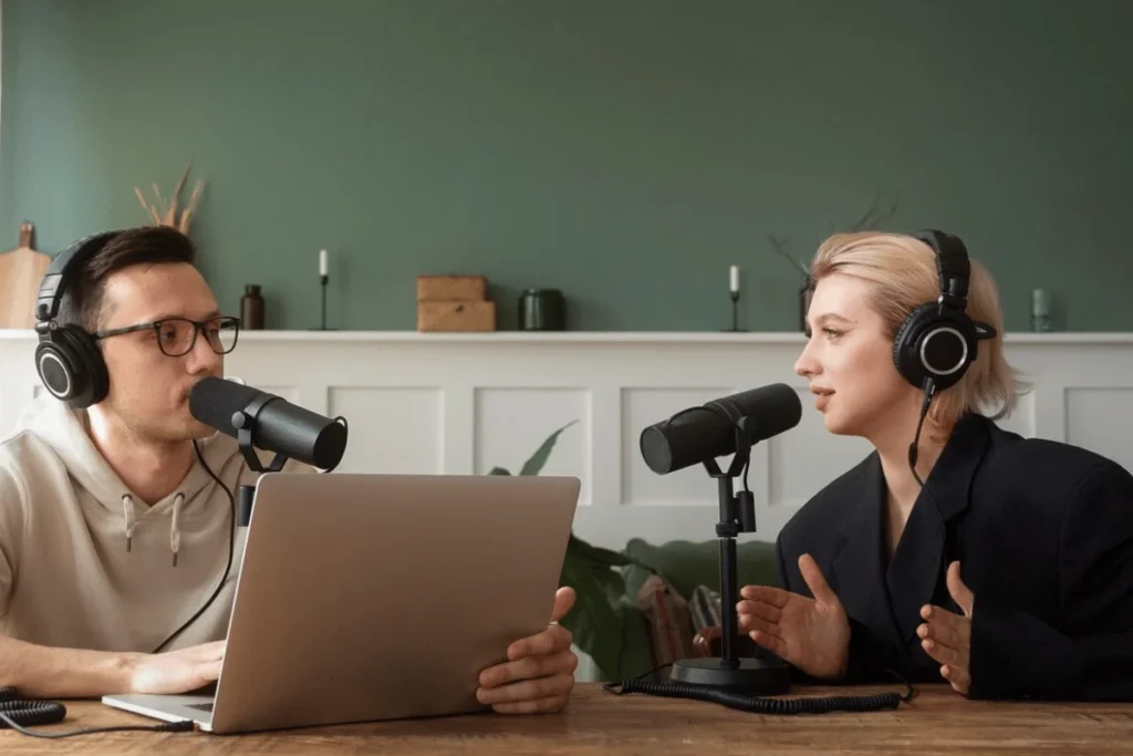 Male and female podcasters engaging in a recording session with professional microphones and a laptop in a cozy studio.