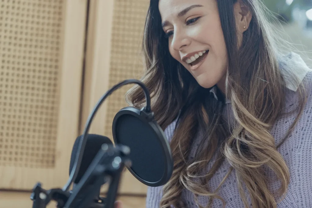 Smiling woman speaking into a microphone during a podcast recording session.