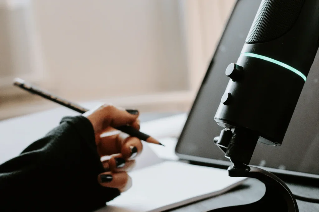 Close-up of a hand holding a pencil near a podcast microphone.