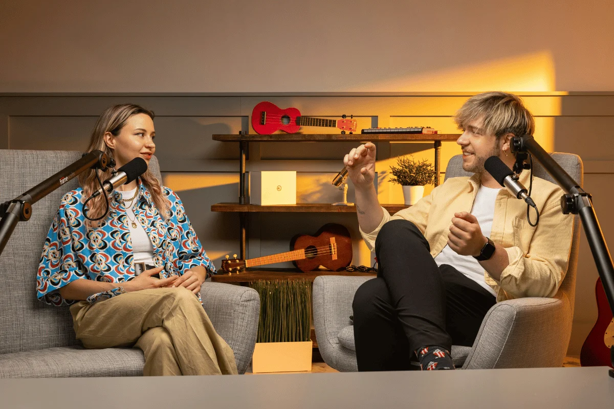 A man and a woman having a conversation during a podcast recording session, surrounded by musical instruments.