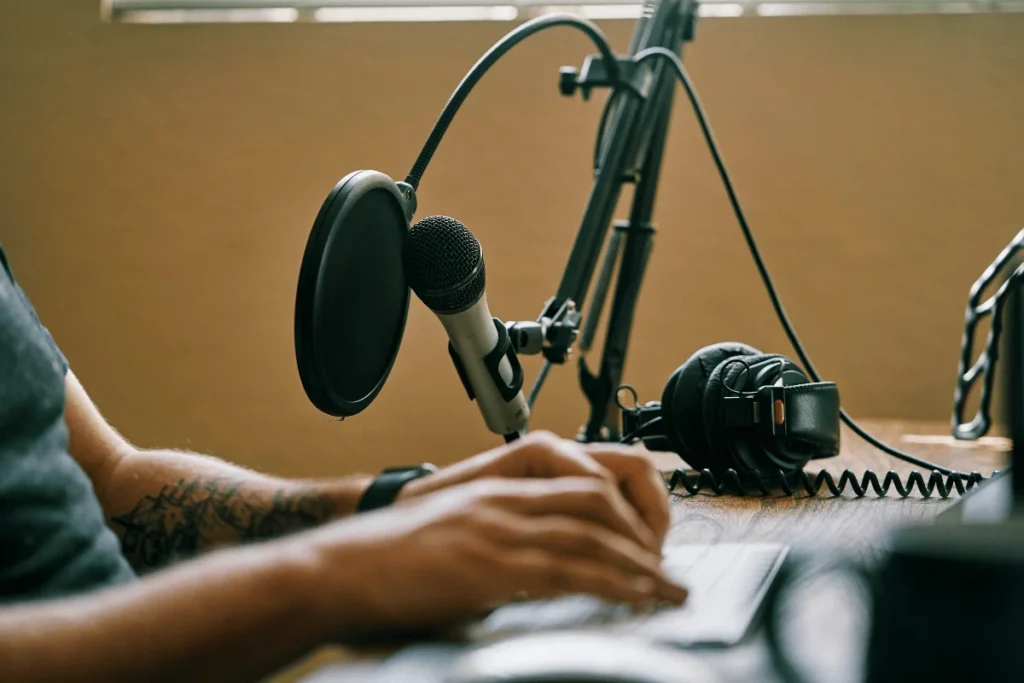 Podcaster typing on a keyboard with a microphone and headphones set up for recording.