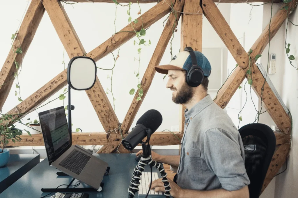 Man with headphones and a microphone, speaking during a podcast session in a cozy, timber-framed room.