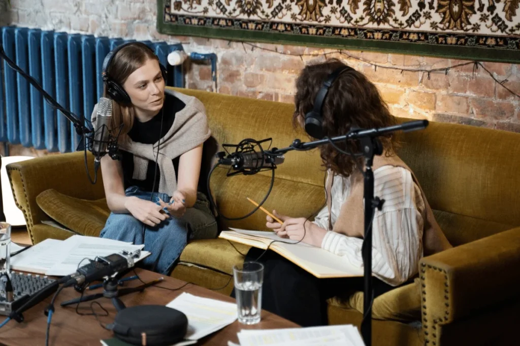 Two women recording a podcast episode in a cozy studio setting with professional microphones and sound equipment.