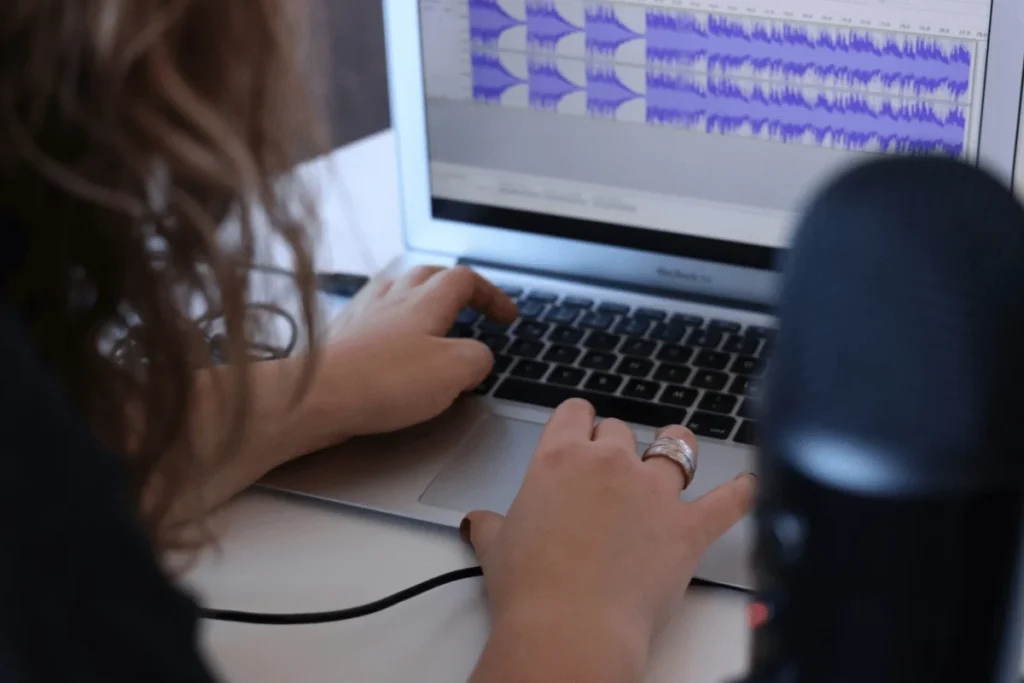 Person editing audio tracks on a laptop with waveforms displayed on the screen.