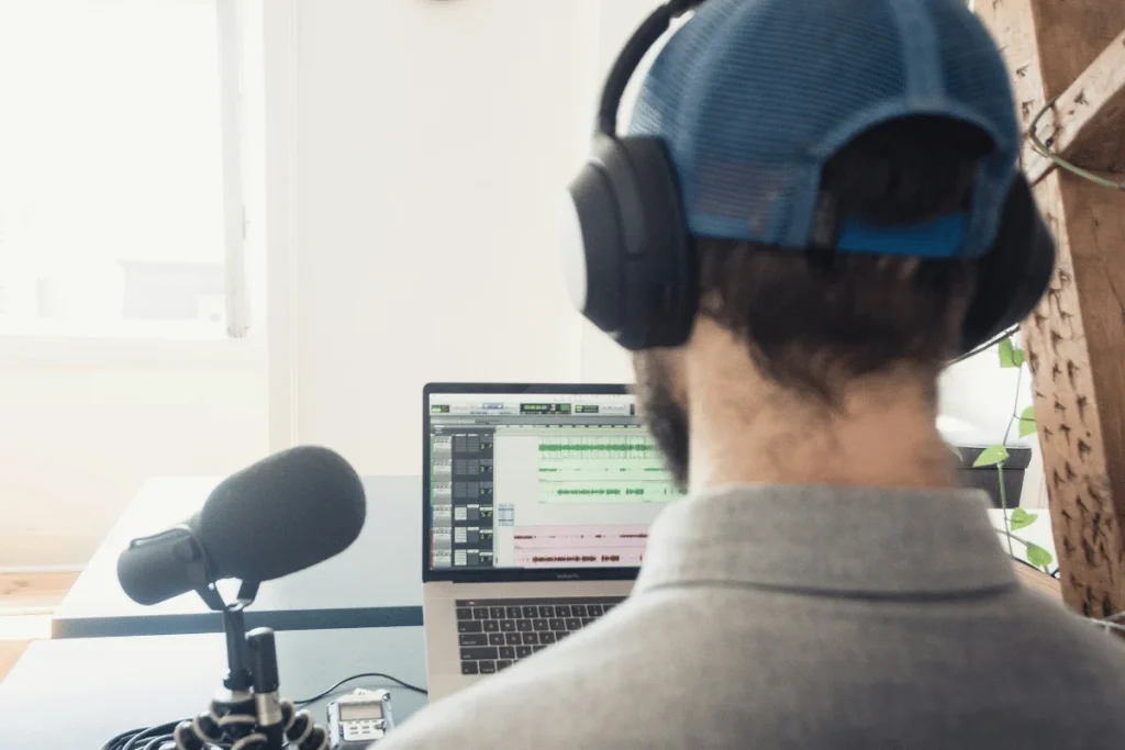 Podcaster using headphones and a professional microphone for audio editing on a laptop.