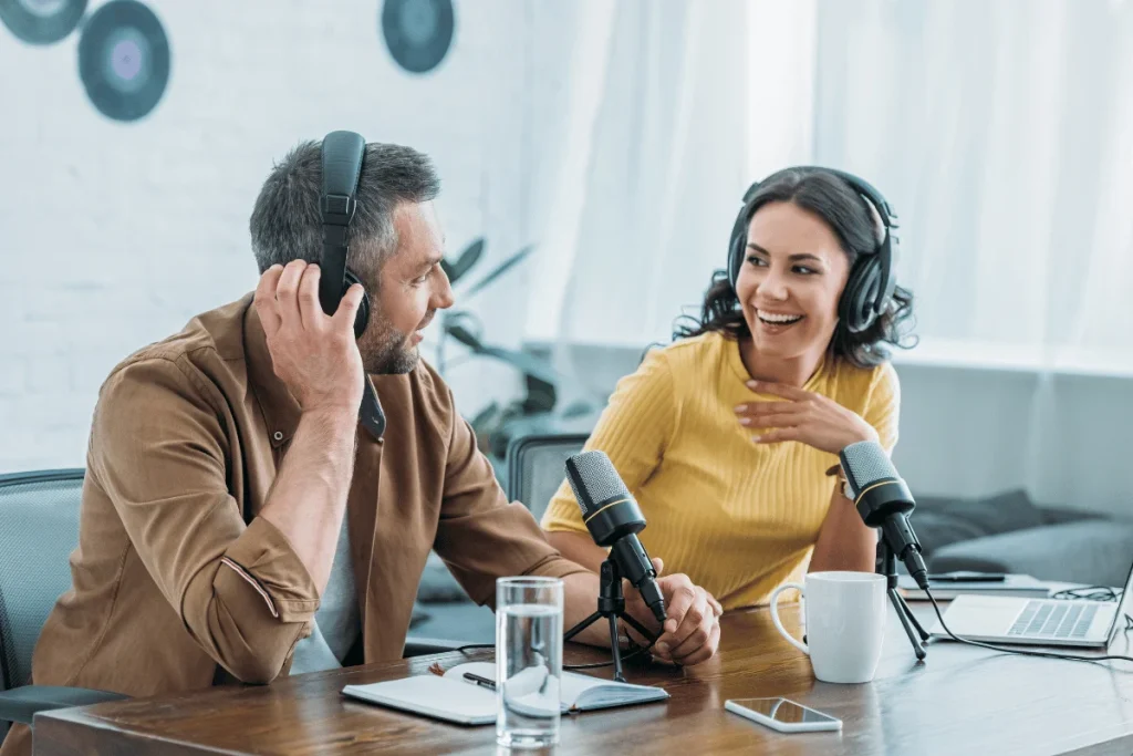 Two podcast hosts smiling and recording together with microphones.