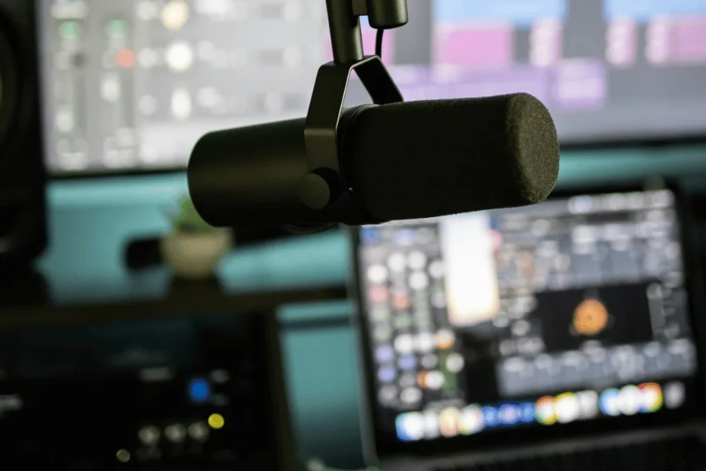 Close-up of a professional microphone with a laptop displaying audio editing software in the background.