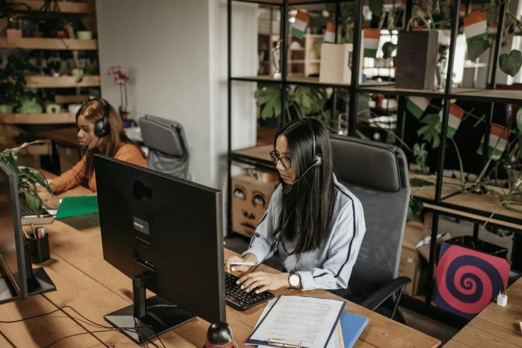 Employees with headsets working diligently at desks in an office with plants.