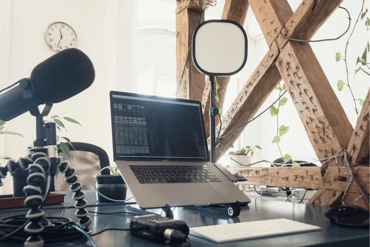 Professional podcasting station featuring a laptop, microphone, lighting, and audio equipment in a well-lit office space.