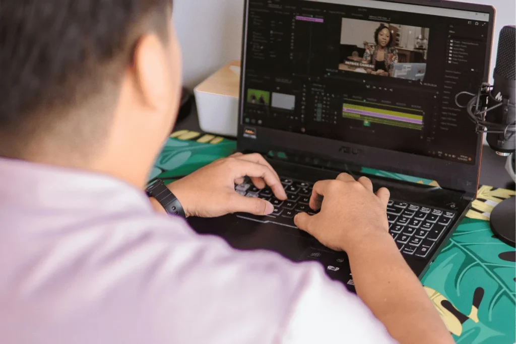 Video editor working on a project on a laptop with a microphone, creating content in a home office.