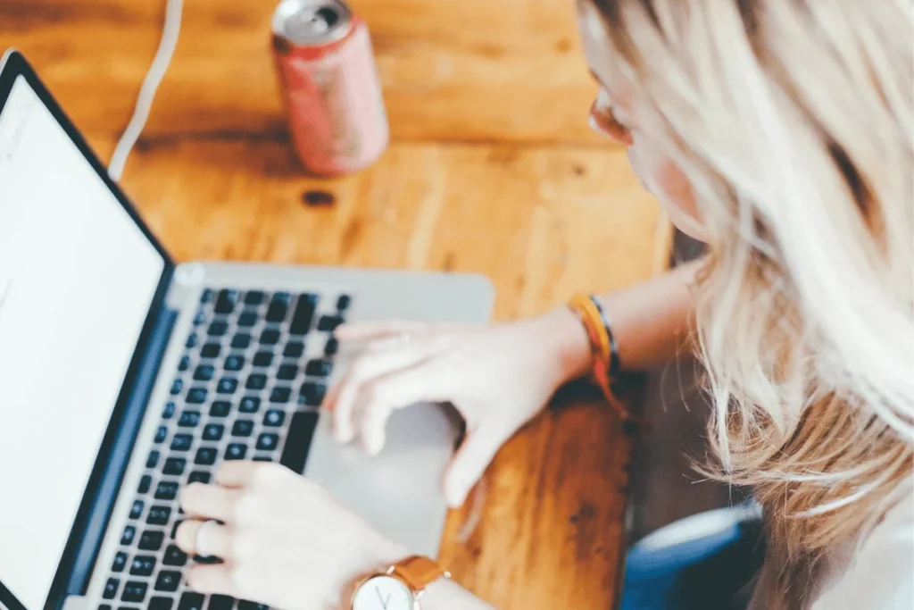 Overhead view of a woman working on a laptop with a soda can nearby.