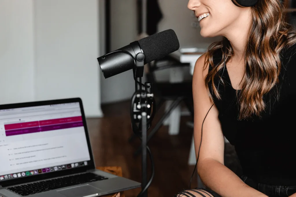 Happy content creator recording a podcast on a laptop with a microphone.