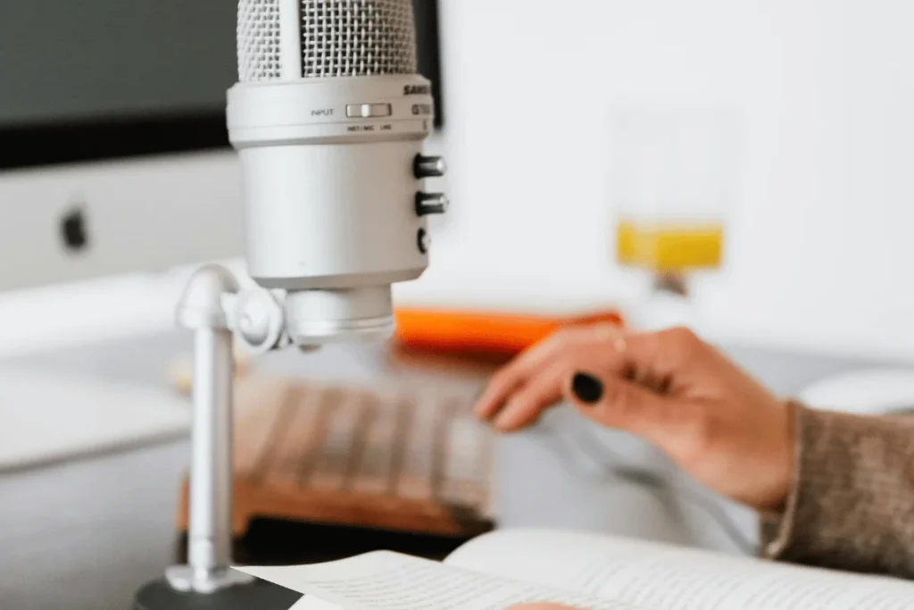 Silver microphone on a stand with a blurred background of a person working on a computer.