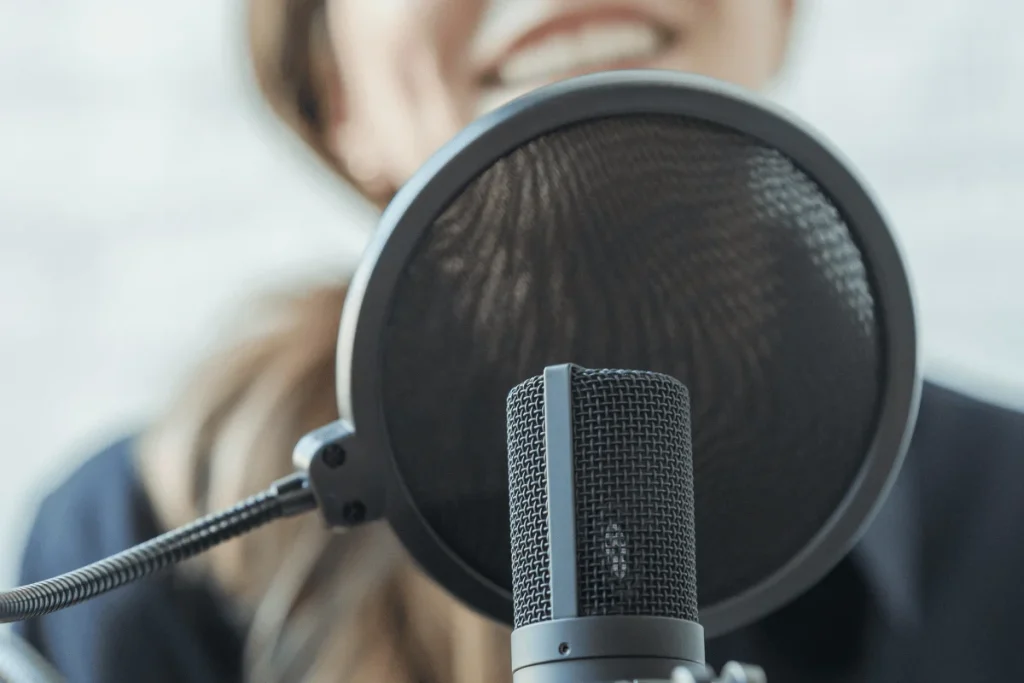 Close-up of a microphone with a pop filter in front of a person speaking.