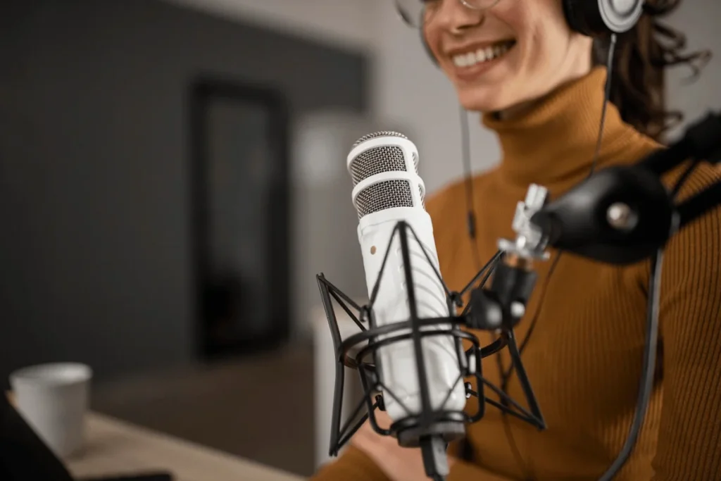 Smiling podcaster with a white microphone and headphones during a recording session.