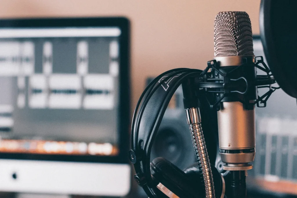 Close-up of a high-quality microphone and headphones in front of a computer with audio tracks.