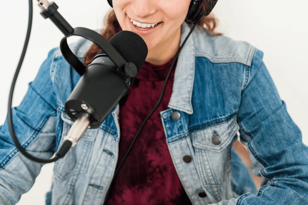 Broadcaster in denim jacket recording with a black studio microphone.