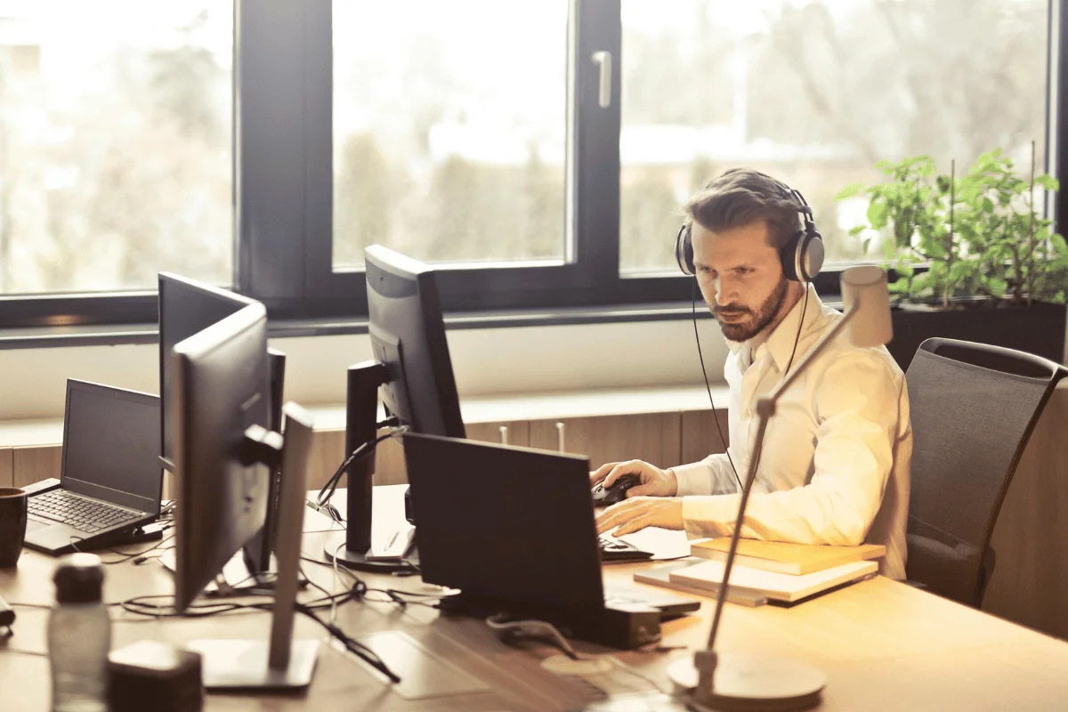 Serious office worker at desk with dual screens and wearing over-ear headphones.