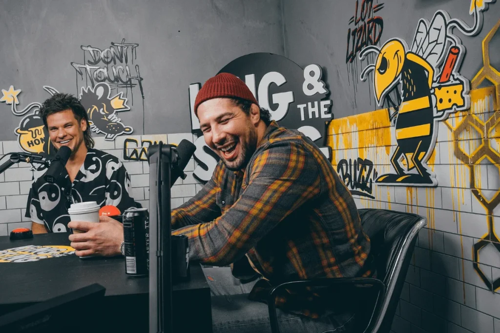 Energetic podcast discussion with two hosts, surrounded by vibrant wall art and microphones.