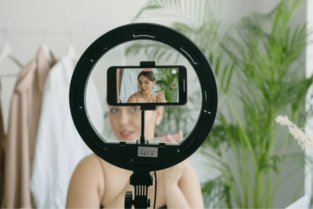 Woman recording a beauty tutorial using a smartphone and ring light.