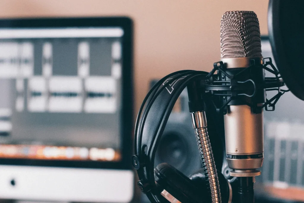 Close-up of a microphone and headphones in a recording studio with a computer monitor displaying audio software.