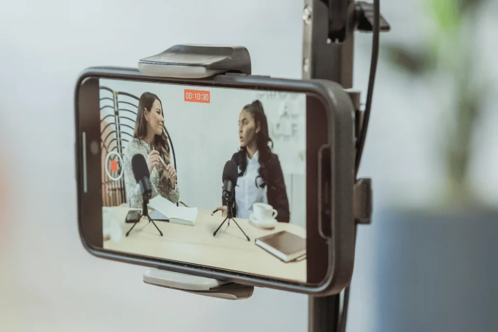 Smartphone recording two people in a podcast setup with a microphone and notes.