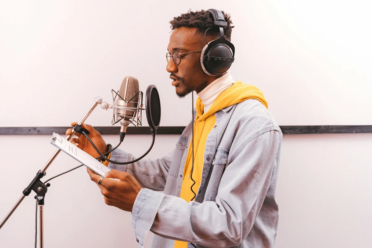 Man wearing headphones recording voiceover in studio with microphone.