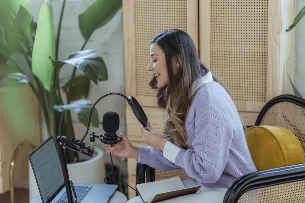 Female podcaster speaking into a microphone while looking at a laptop.