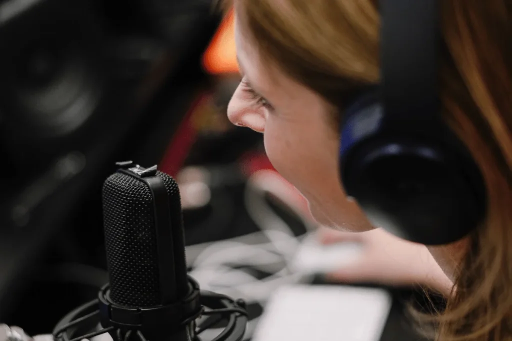 Side profile of a woman with headphones recording at a studio microphone.