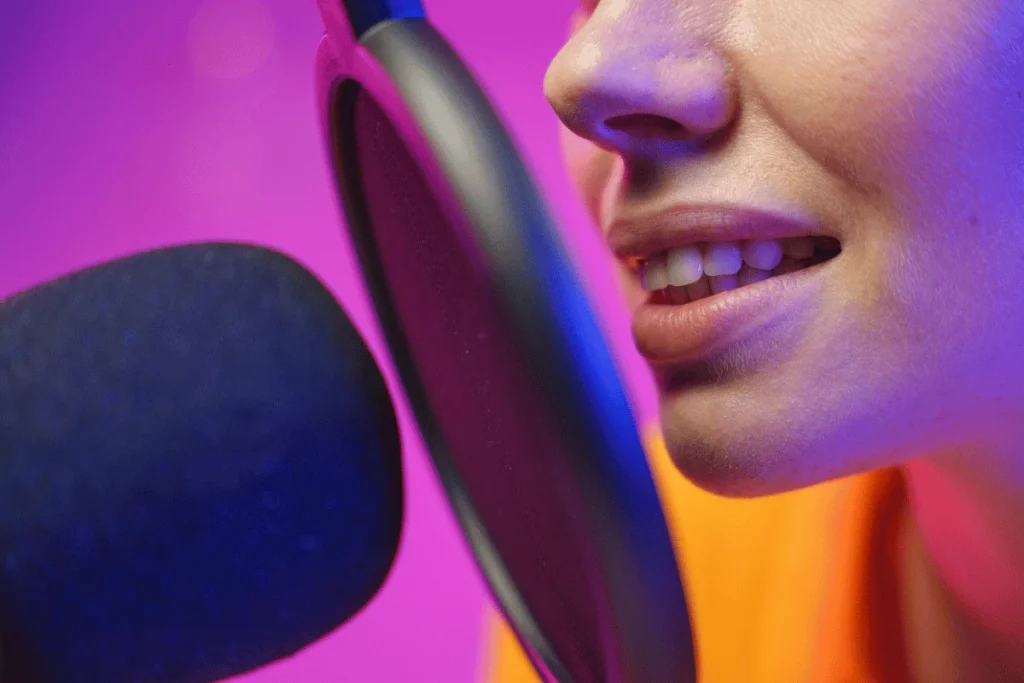 Close-up of a woman speaking into a microphone with a pop filter, highlighting clear audio recording in a vibrant studio setting.