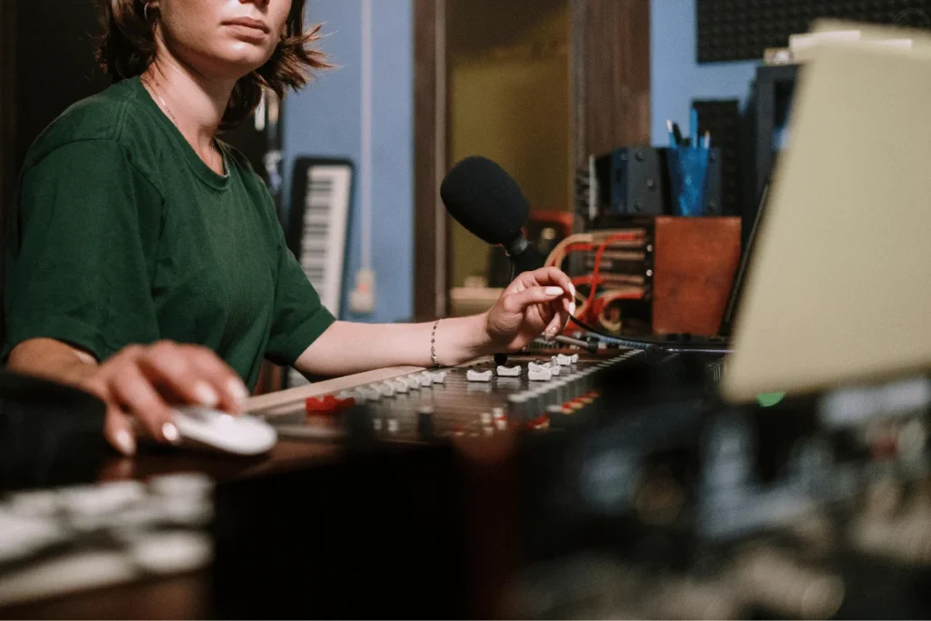 Audio engineer operating a mixing console in a recording studio, adjusting levels and working with a microphone nearby.