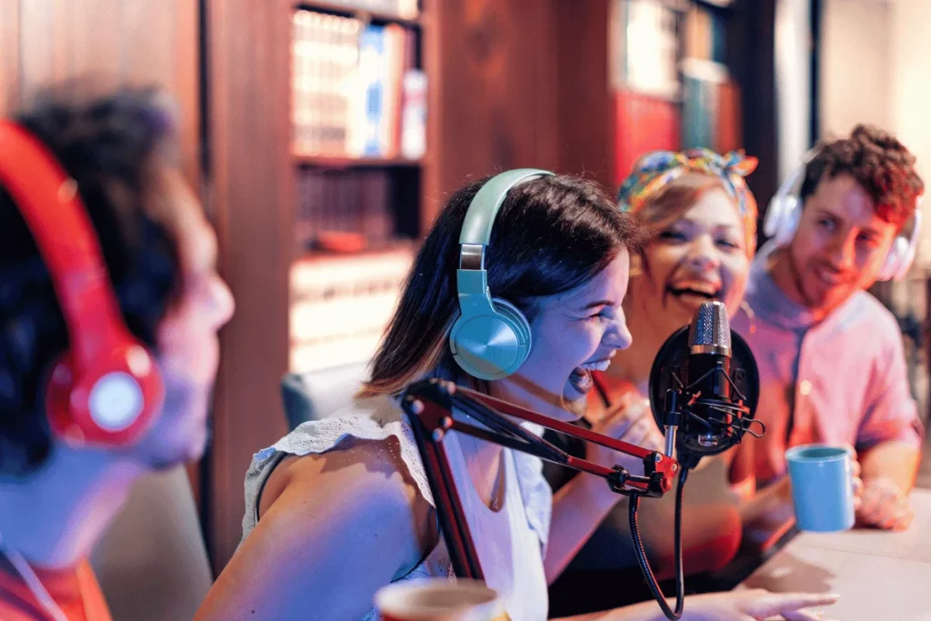 Friends wearing headphones, recording a podcast with a mic in a cozy studio.