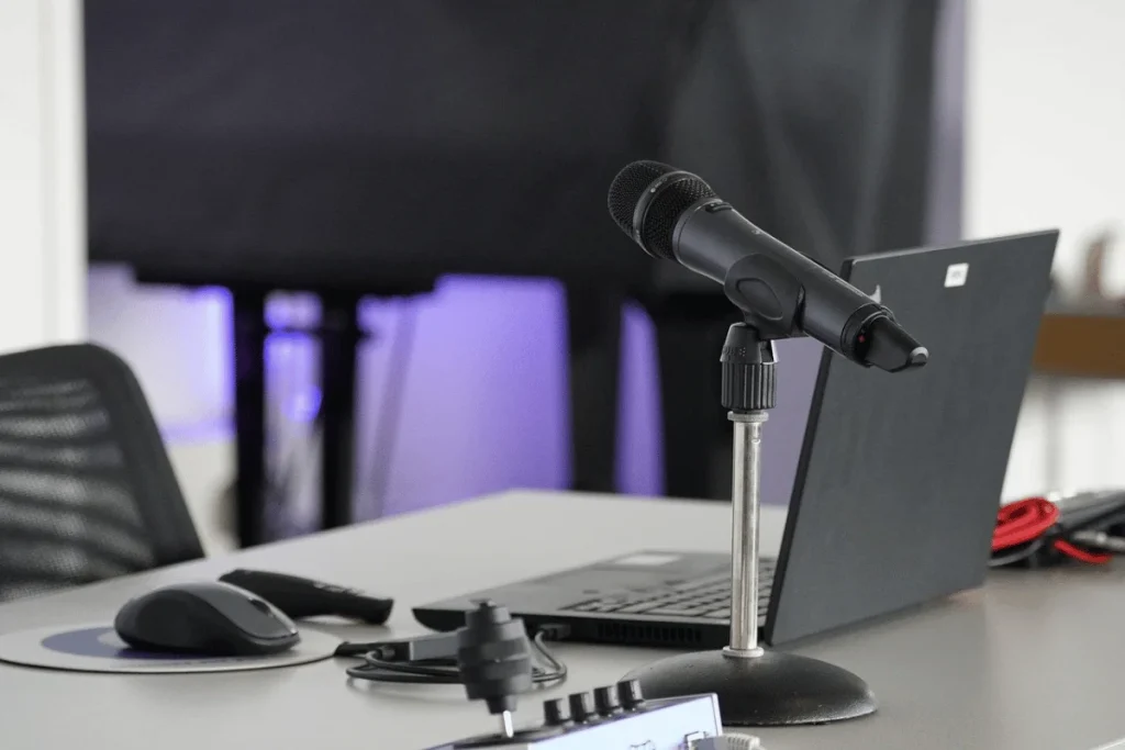 Podcasting setup with a black microphone and laptop on a desk, professional office background.