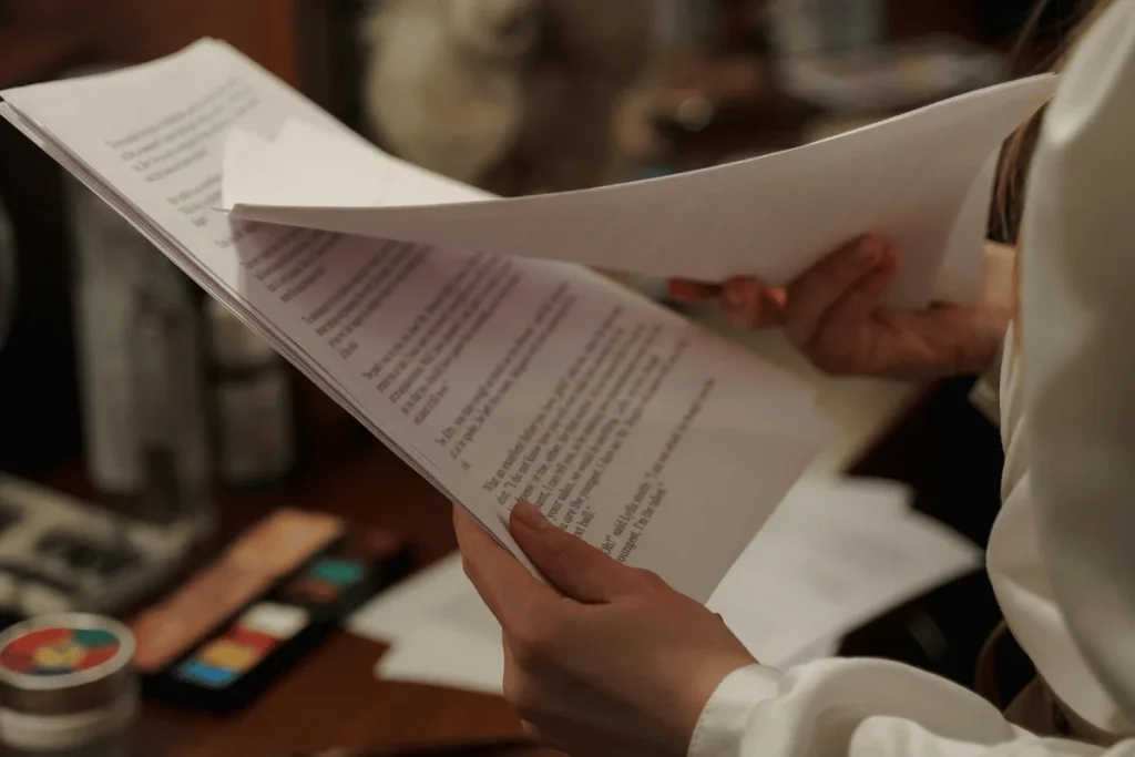 Person holding and flipping through several pages of printed text, engaged in document review or script reading.