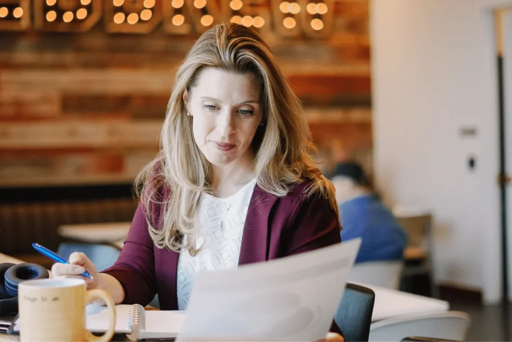 Nora Sudduth focused on paperwork in a café with festive lights.