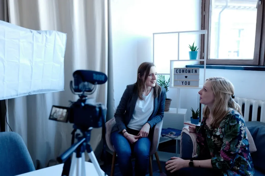 Two women having a conversation during a video shoot in a cozy room.