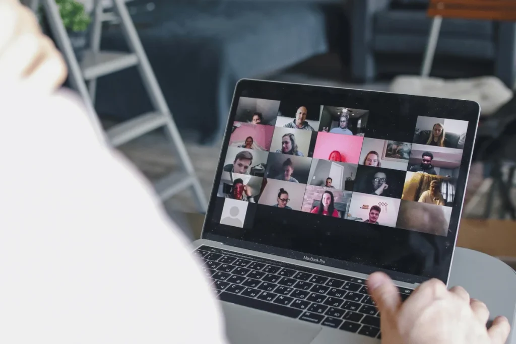 A person attends a virtual meeting on a laptop, displaying multiple video thumbnails of participants in a grid format.
