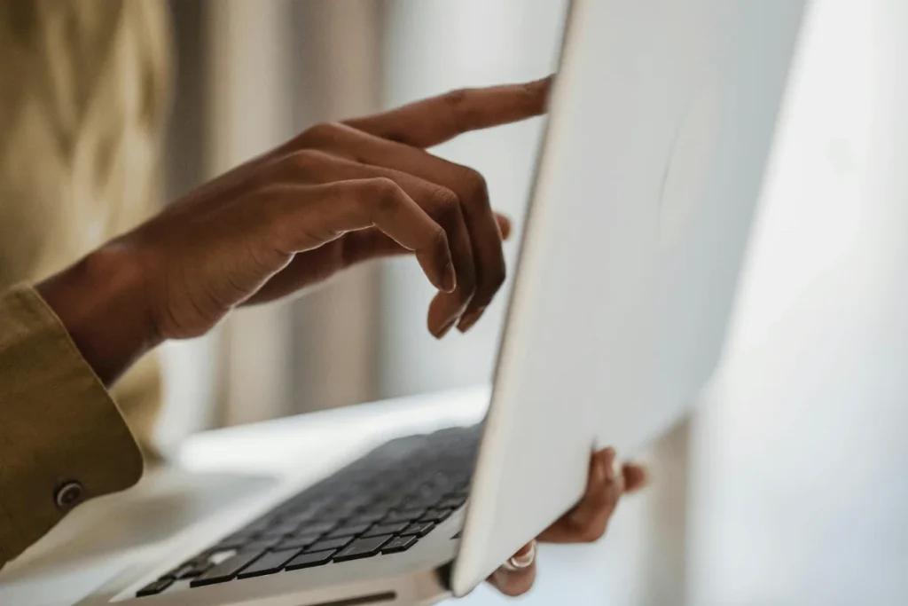 Fingers of a user lifting the lid of a sleek, white laptop.