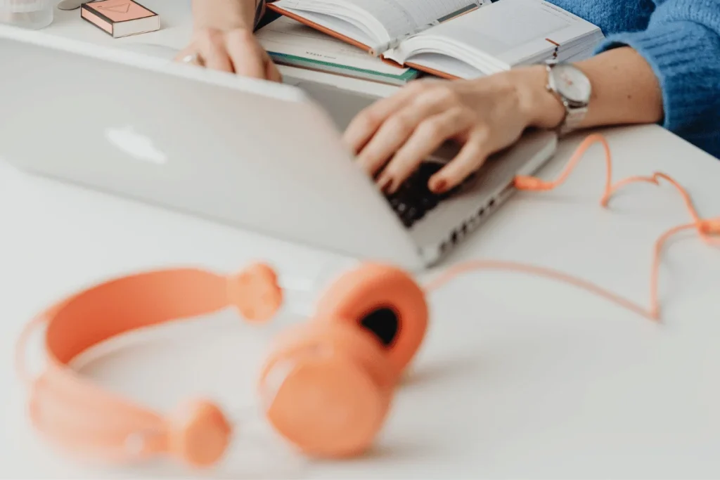 Casual laptop use with trendy orange headphones and a book.