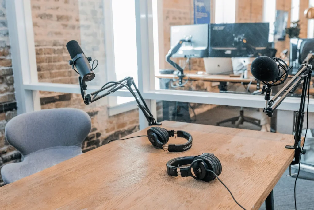 Empty podcast studio setup with microphones and headphones on a wooden table.