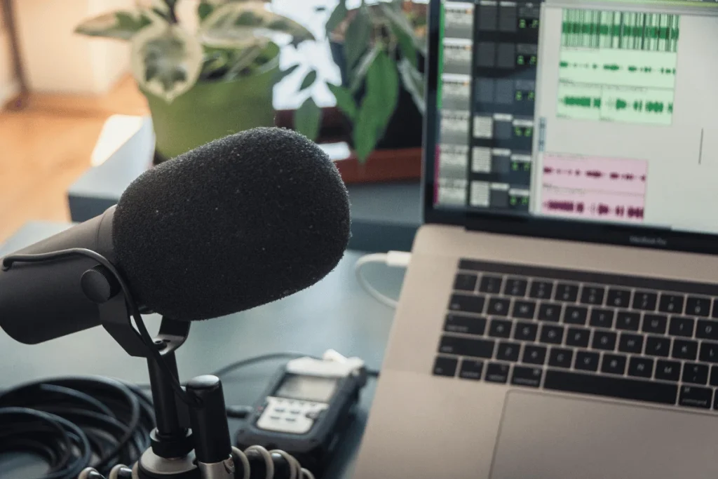 Podcasting microphone setup in a home studio with a laptop showing audio tracks on the screen.