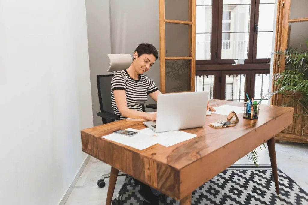 Content woman typing on a laptop at a wooden desk with a relaxed posture.