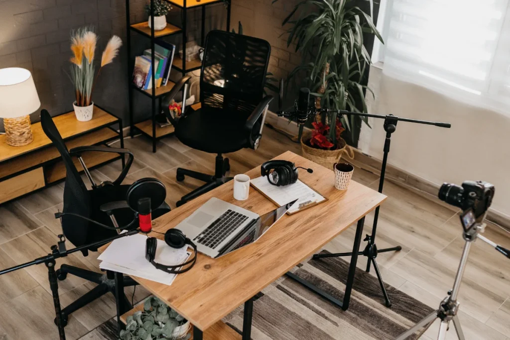 A modern podcast studio setup featuring microphones, headphones, a laptop, and cameras in a well-lit creative workspace.