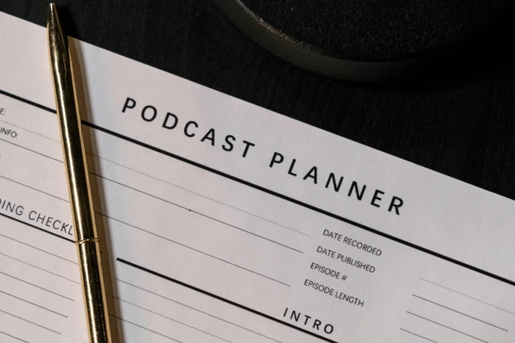 Gold pen resting on a podcast planner sheet, highlighting sections for date recorded, date published, and episode details.