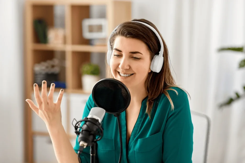 Woman in green top with headphones speaking into a microphone, gesturing with hand.