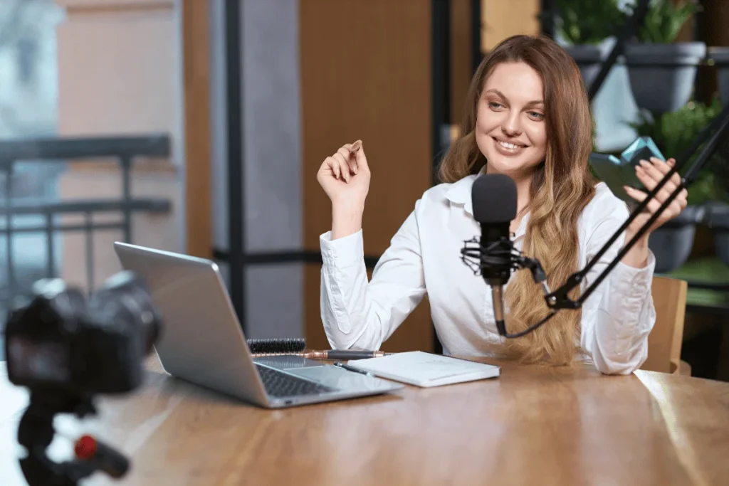 Person recording a podcast with a microphone and laptop, camera in the foreground.