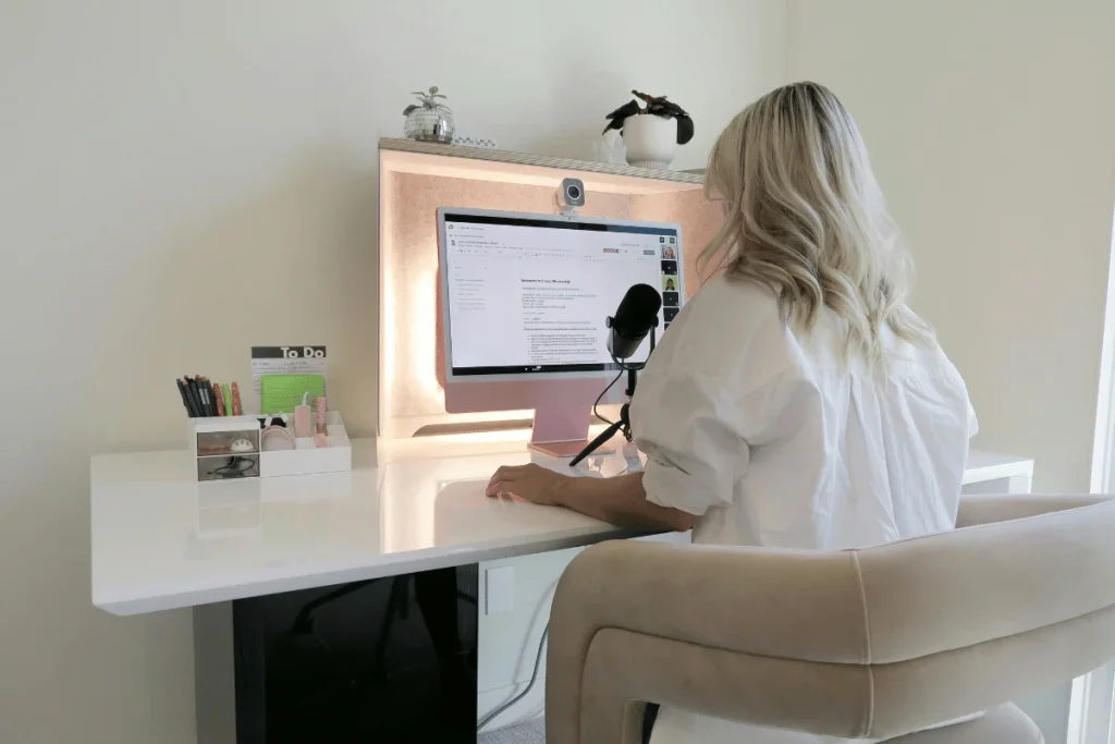 Woman at a modern home office desk with a computer and podcasting microphone.