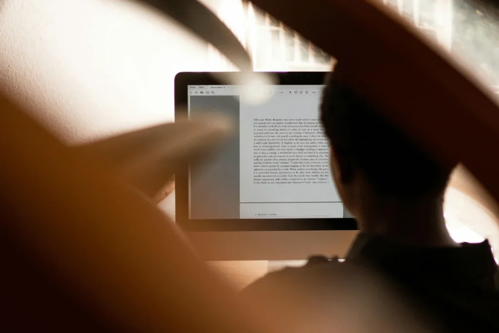 A person reading text on a computer screen, framed by soft, blurred foreground elements.