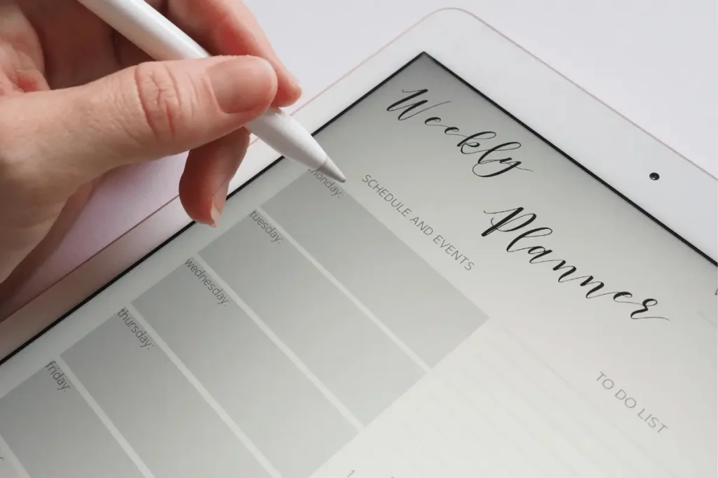 Hand using a stylus to write on a digital weekly planner.